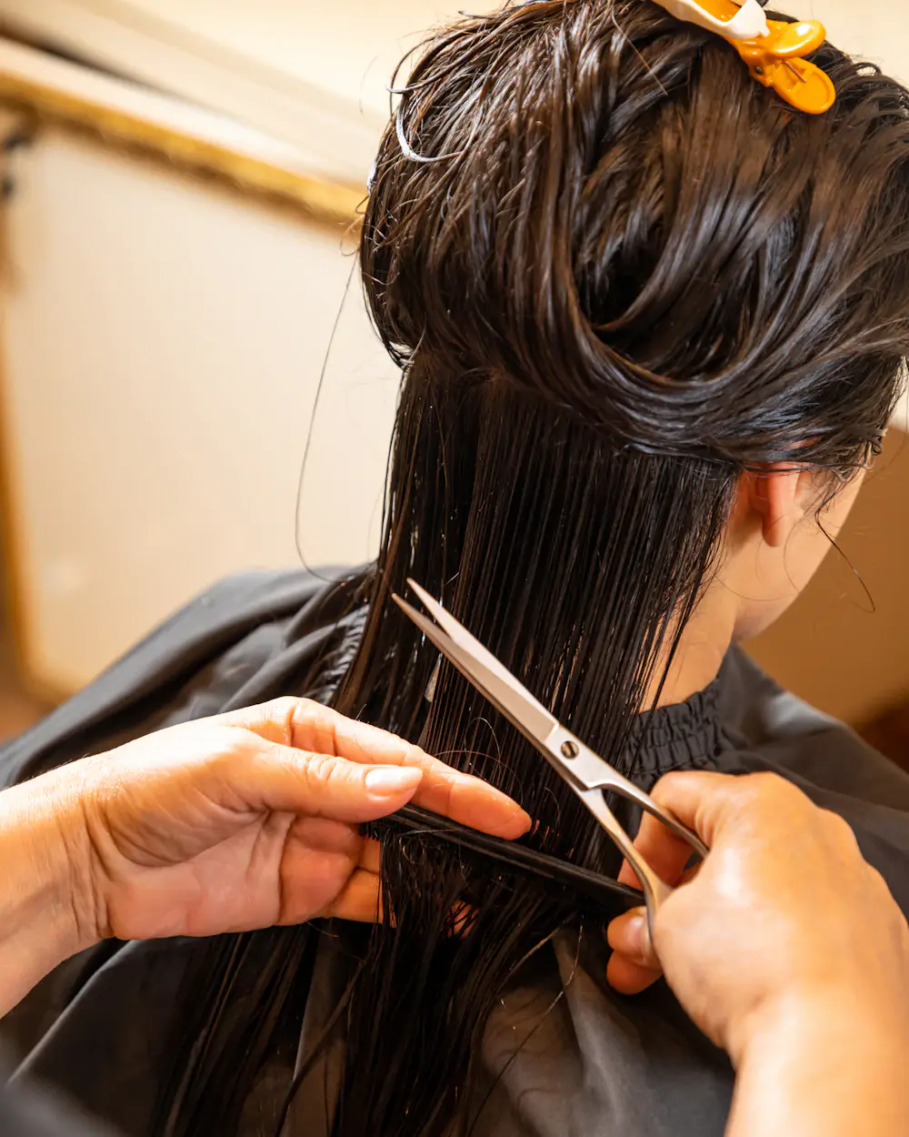 Cabeleireira separando uma mecha por dentro do cabelo e cortando com tesoura